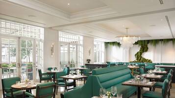 A restaurant with green upholstered booths and tables, large windows, and a chandelier.