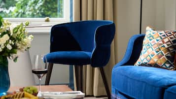 A blue sofa with a patterned pillow, a vase with flowers, and a glass of red wine on a table.