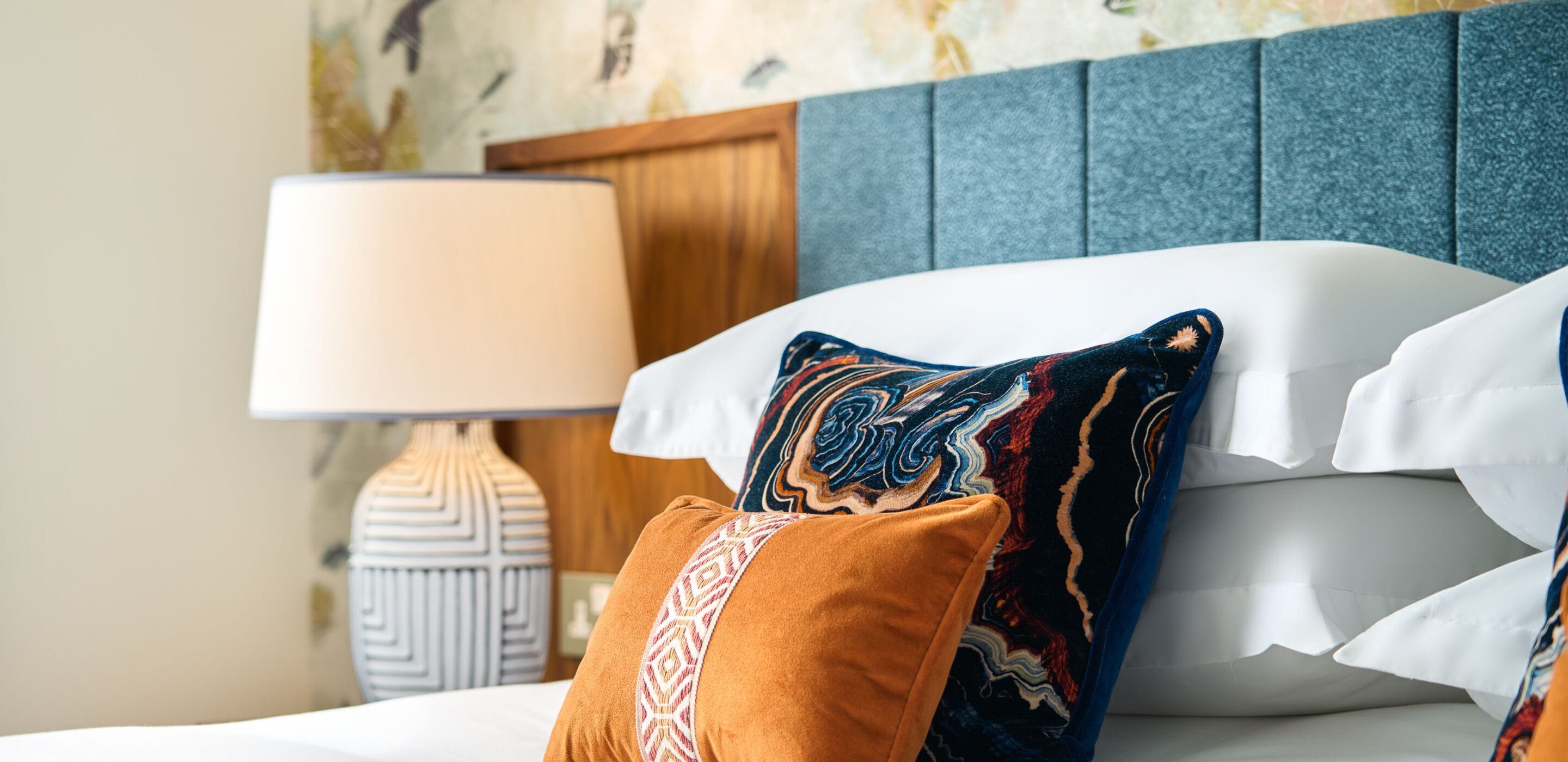A neatly made bed with patterned pillows, a bedside lamp, and a decorative wall.