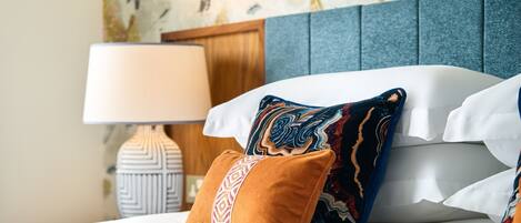 A neatly made bed with patterned pillows, a bedside lamp, and a decorative wall.