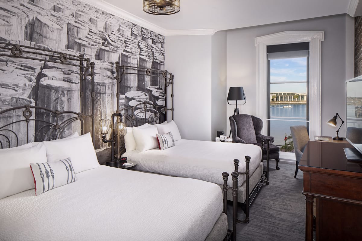 A hotel room with two beds, a desk, a chair, and a view of the water.