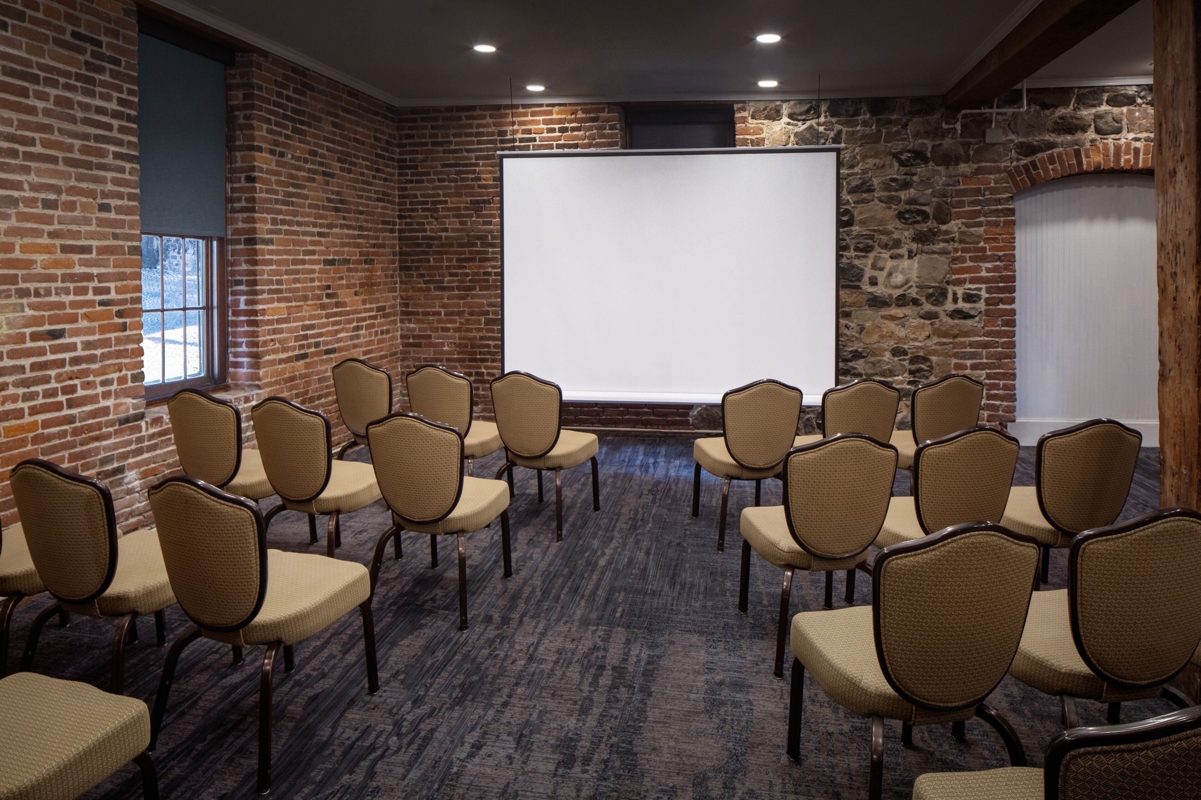 Ein Konferenzraum mit einer Wandtafel, Backsteinwänden und Reihen beige farbener Stühle.