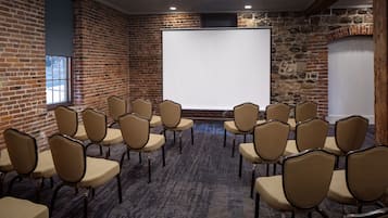 Ein Konferenzraum mit einer Wandtafel, Backsteinwänden und Reihen beige farbener Stühle.