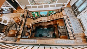 A spacious lobby with a wooden staircase, a fireplace, and a large mural on the ceiling.