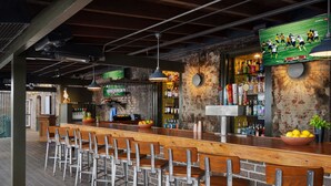 A bar area with wooden bar stools, a long counter, and a television displaying a sports game.