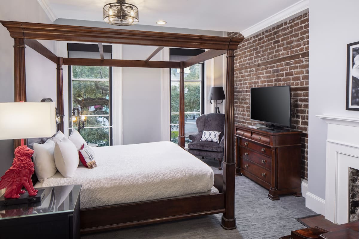 A bedroom with a four-poster bed, a dresser, a television, and a fireplace.
