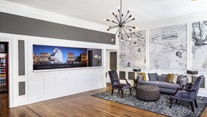 A spacious living room with a large flat-screen TV, a modern chandelier, and a large map on the wall.