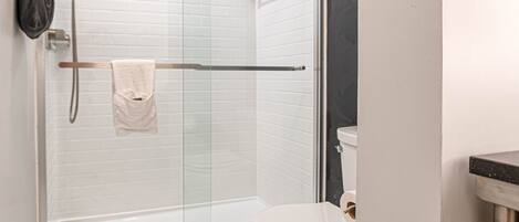 A modern bathroom with a glass-enclosed shower, a toilet, and marble flooring.