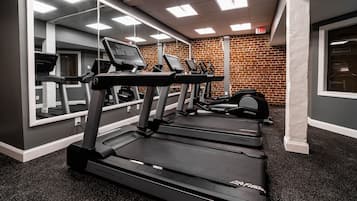 A gym with treadmills, a mirrored wall, and a brick wall.