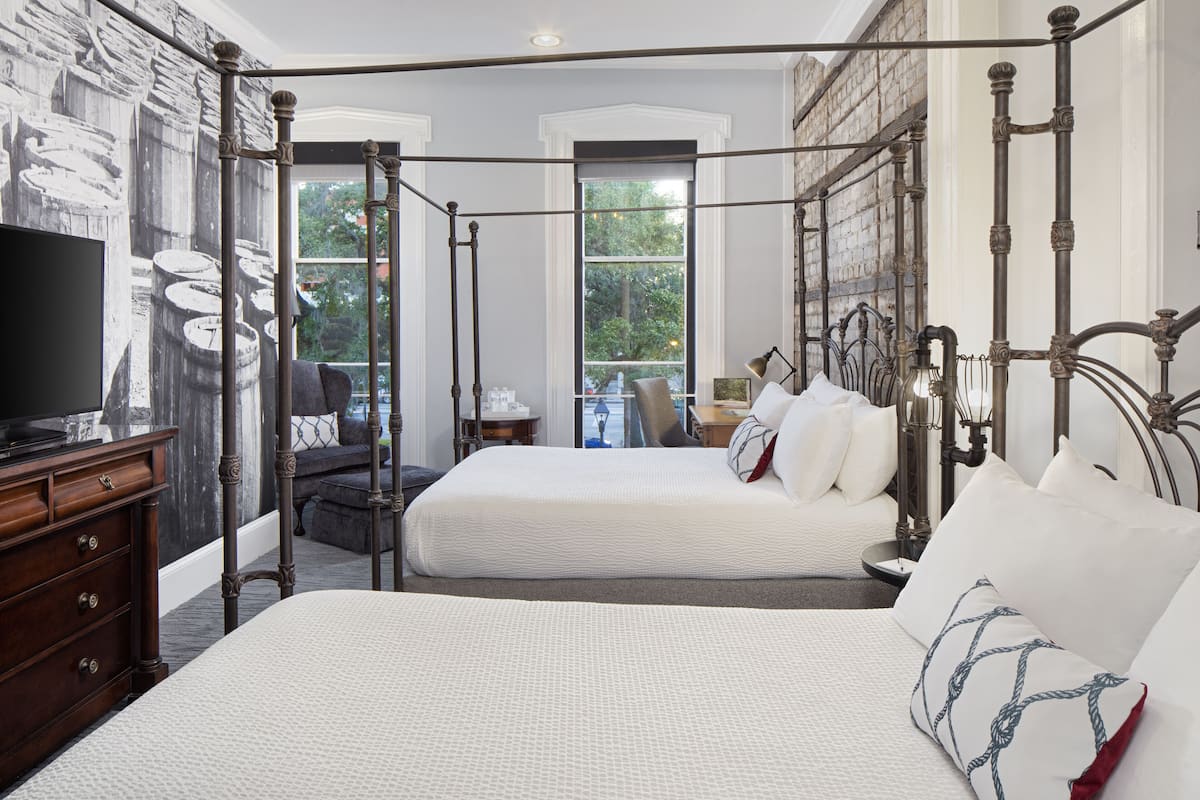A four-poster bed with white bedding, a television on a wooden dresser, and a mural of barrels on the wall.