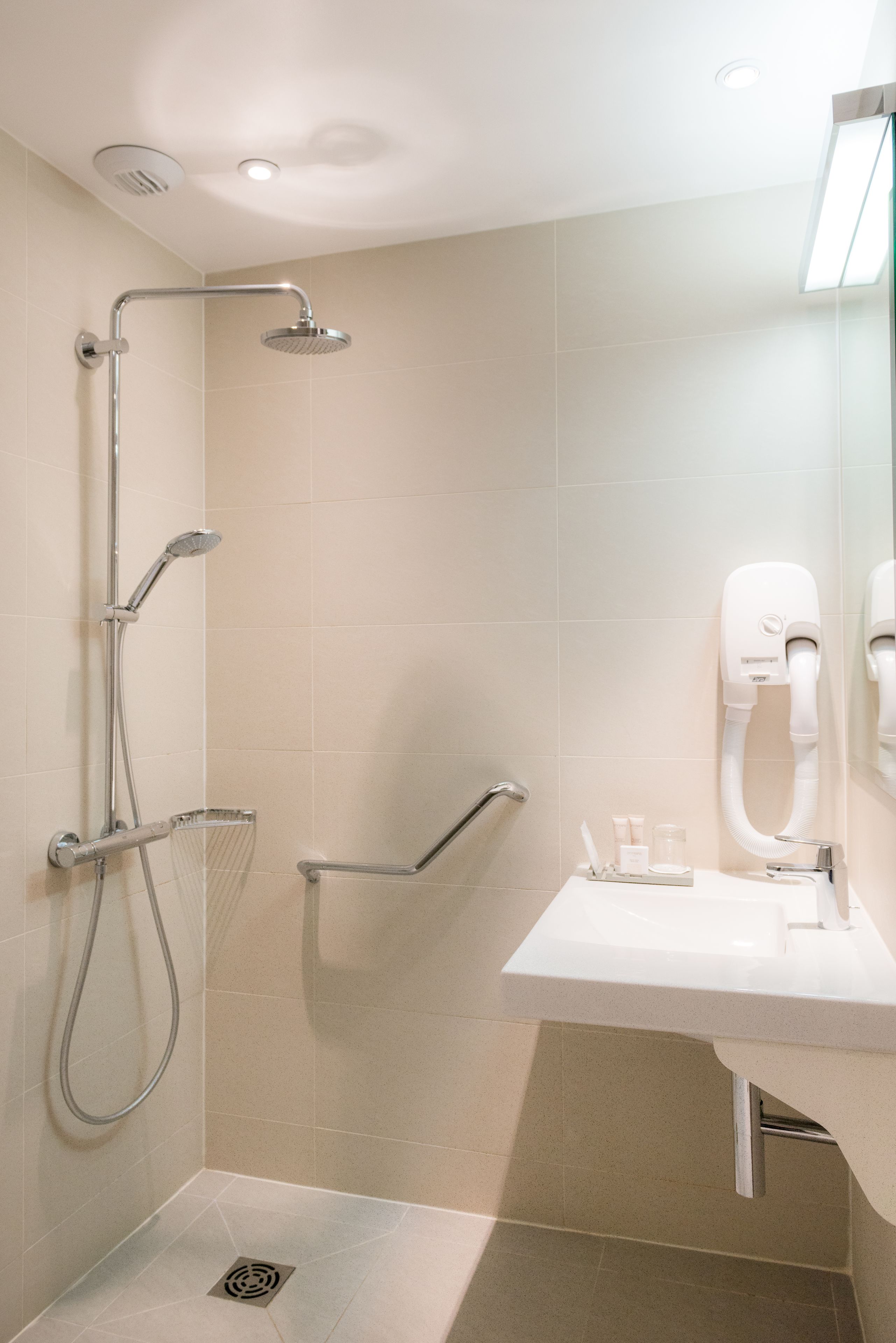 A modern bathroom with a shower, grab bar, and a sink with a mirror.