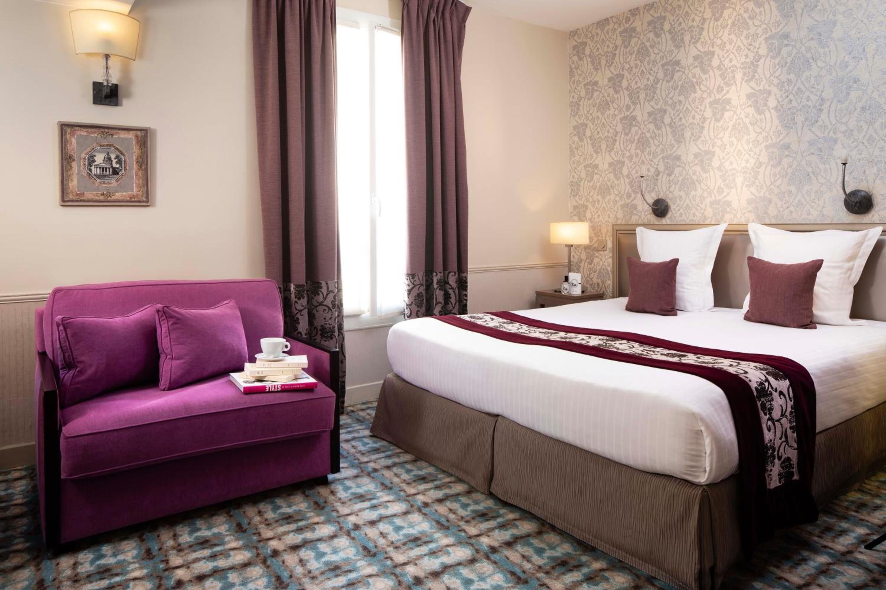Een hotelkamer met een groot bed, een paarse bank en een kamerbreed tapijt met dessin.