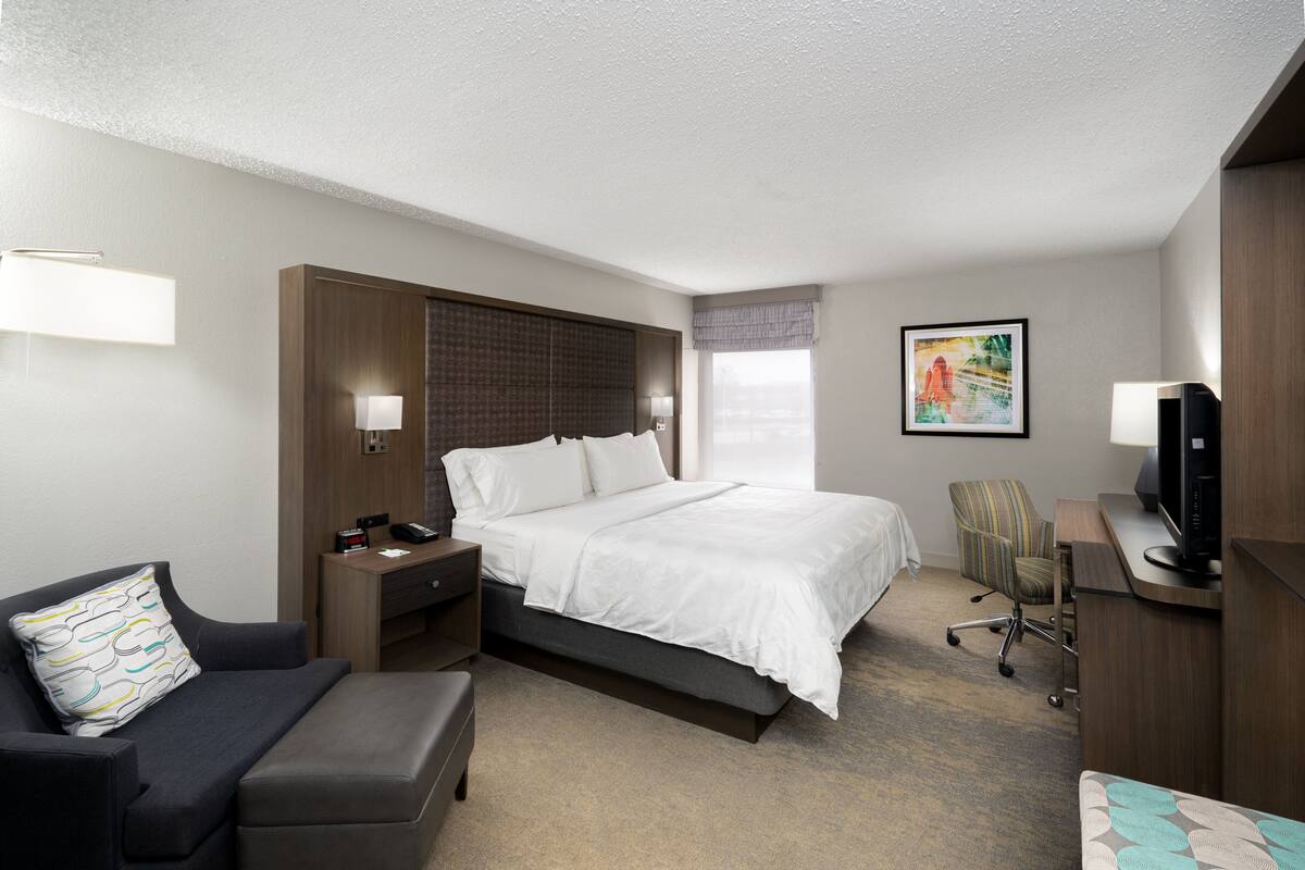 A hotel room with a bed, a desk, a chair, a TV, and a lamp.