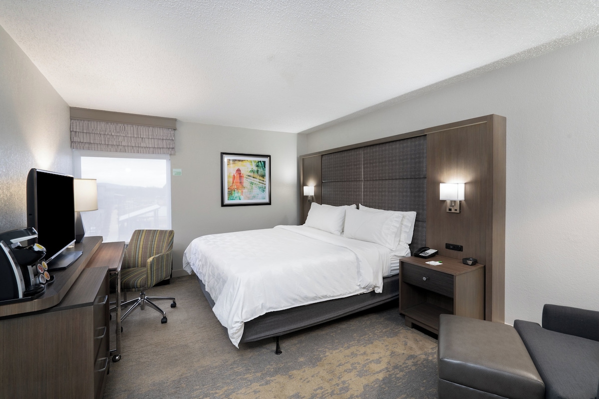A hotel room with a bed, desk, chair, and a television.