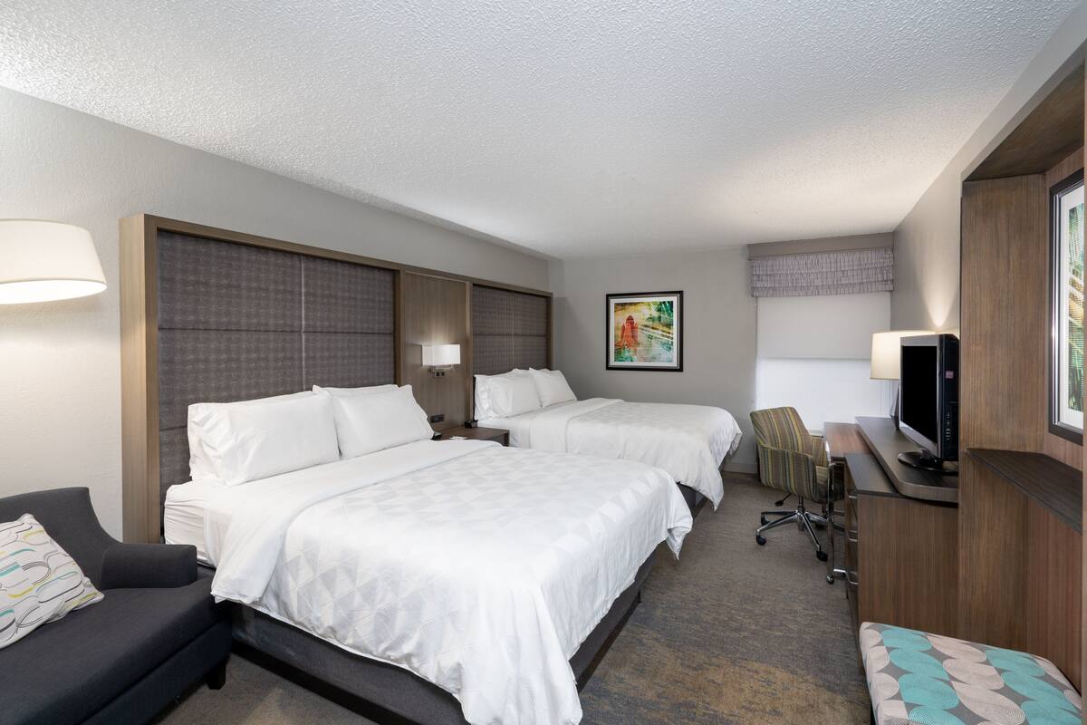 A hotel room with two beds, a desk with a television, a chair, and a couch.