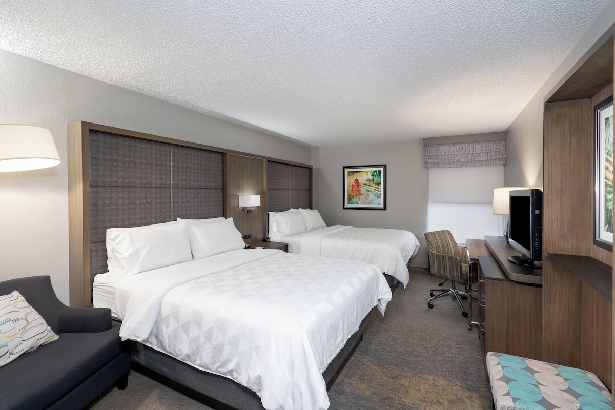 A hotel room with two beds, a desk with a television, a chair, and a couch.
