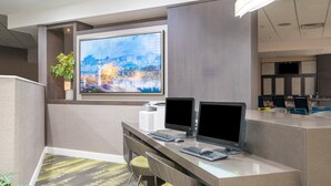 Un mostrador de recepción con dos monitores, una computadora y un cuadro grande de un paisaje urbano.