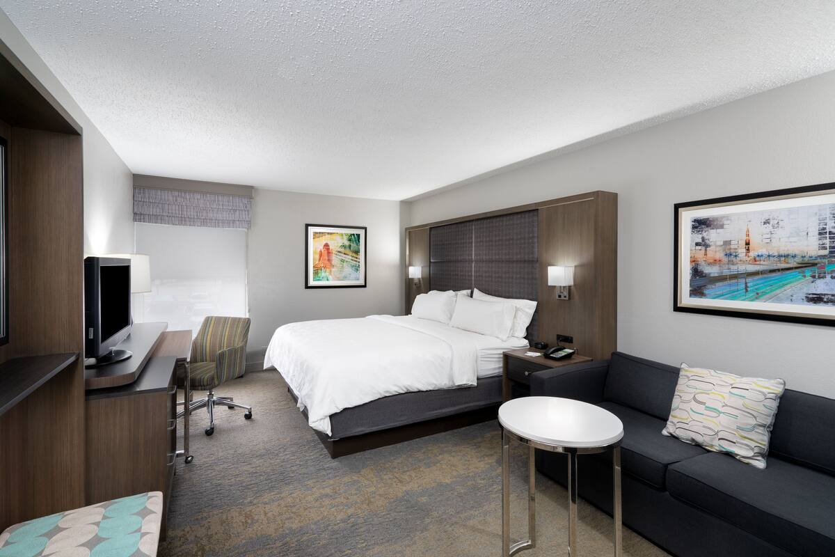 A hotel room with a bed, a desk with a computer, a sofa, and two paintings on the walls.