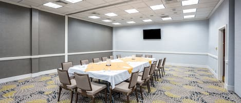 A conference room with a long table, chairs, and a flat-screen TV on the wall.