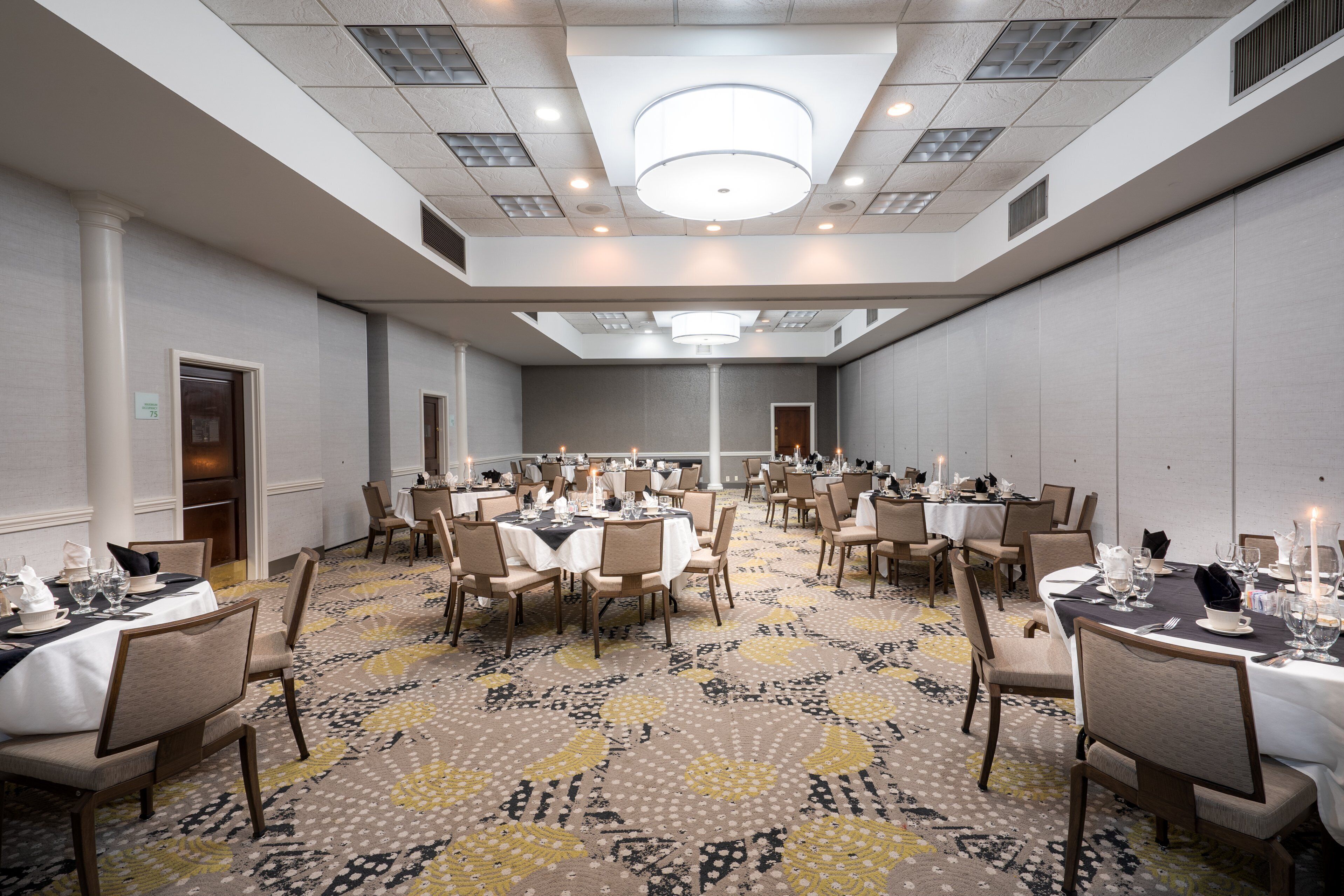 A large conference room with multiple tables set for dining, equipped with chairs and tables, and a patterned carpet.
