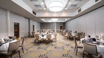 A large conference room with multiple tables set for dining, equipped with chairs and tables, and a patterned carpet.