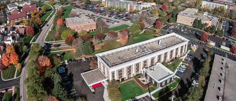 An aerial view of a campus with a central building surrounded by parking lots and greenery.