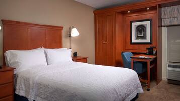 Una habitación de hotel con una cama grande, un escritorio, una silla, una lámpara, un cuadro en la pared y un armario.