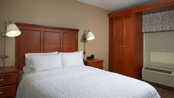A neatly made bed with white bedding, a wooden headboard, two bedside lamps, a nightstand, and a built-in wardrobe with a mirror.
