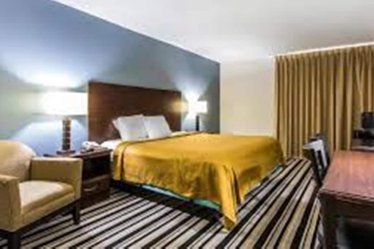 A hotel room with a bed, a chair, a desk, and a lamp.