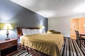 A hotel room with a bed, two bedside lamps, a wooden nightstand, and a striped carpet. - Econo Lodge Ardmore (Ardmore)
