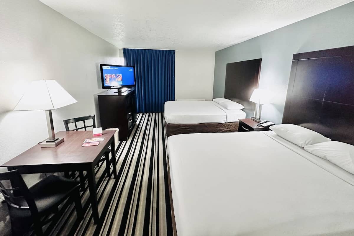 A hotel room with a bed, a desk, a chair, a TV, and a window with curtains.