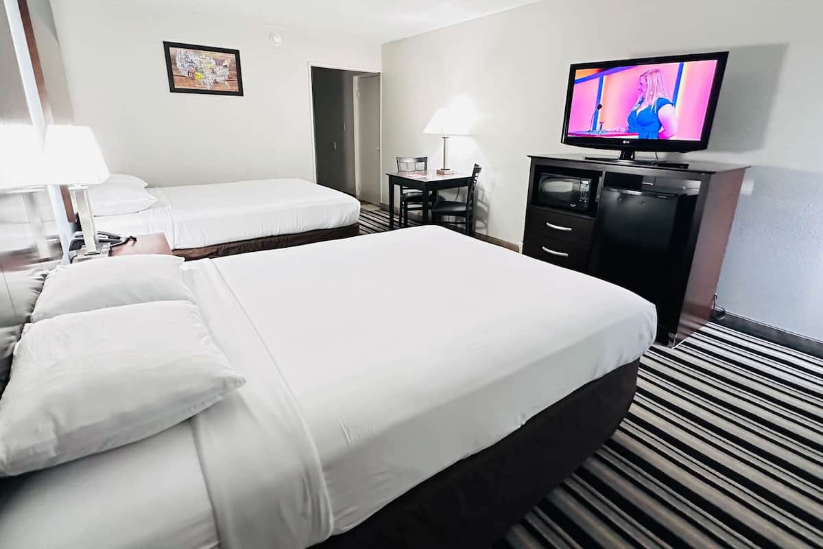 A hotel room with two beds, a television, a desk with a chair, and a lamp.