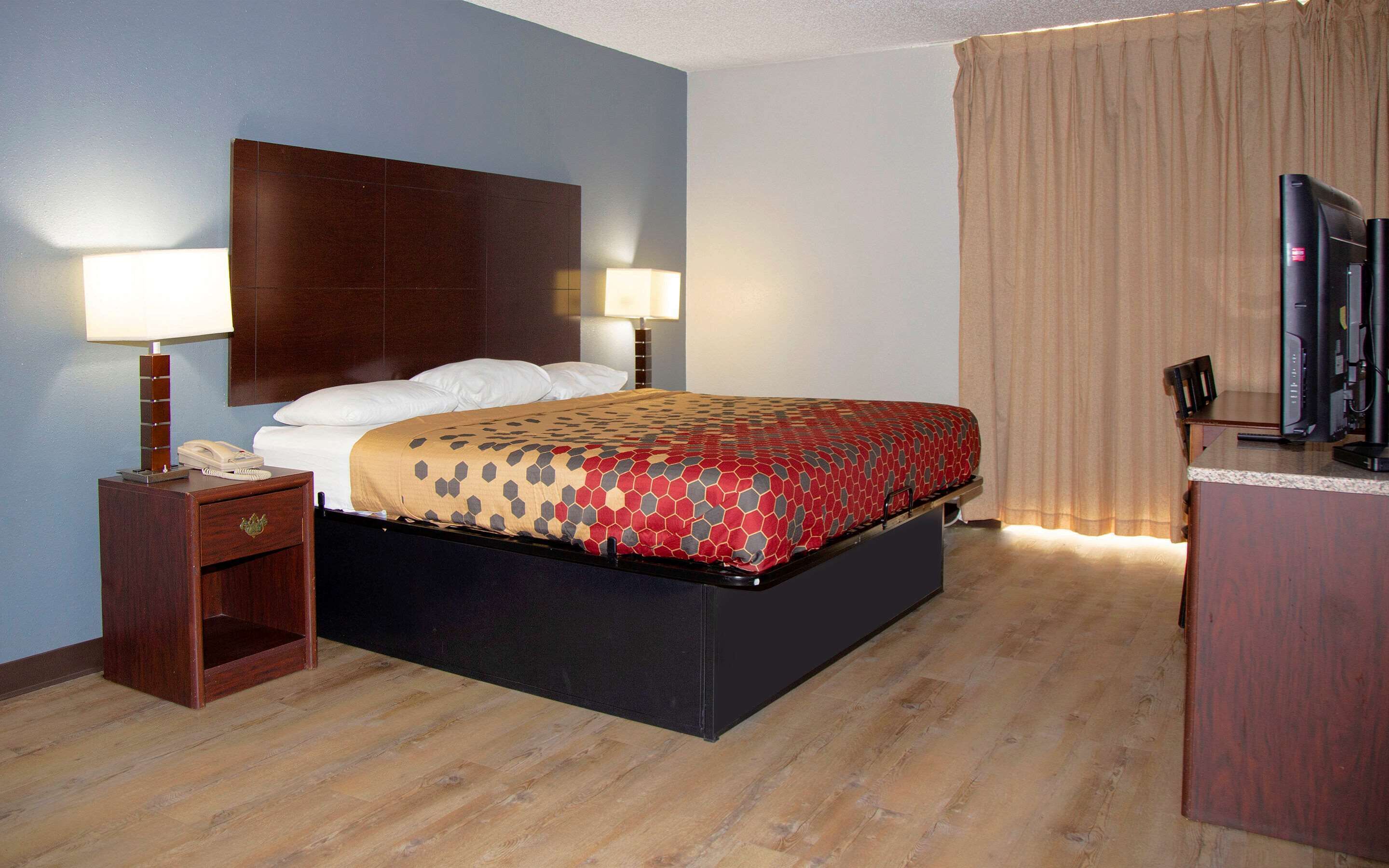 A hotel room with a bed, two bedside lamps, a desk with a computer, and a TV.