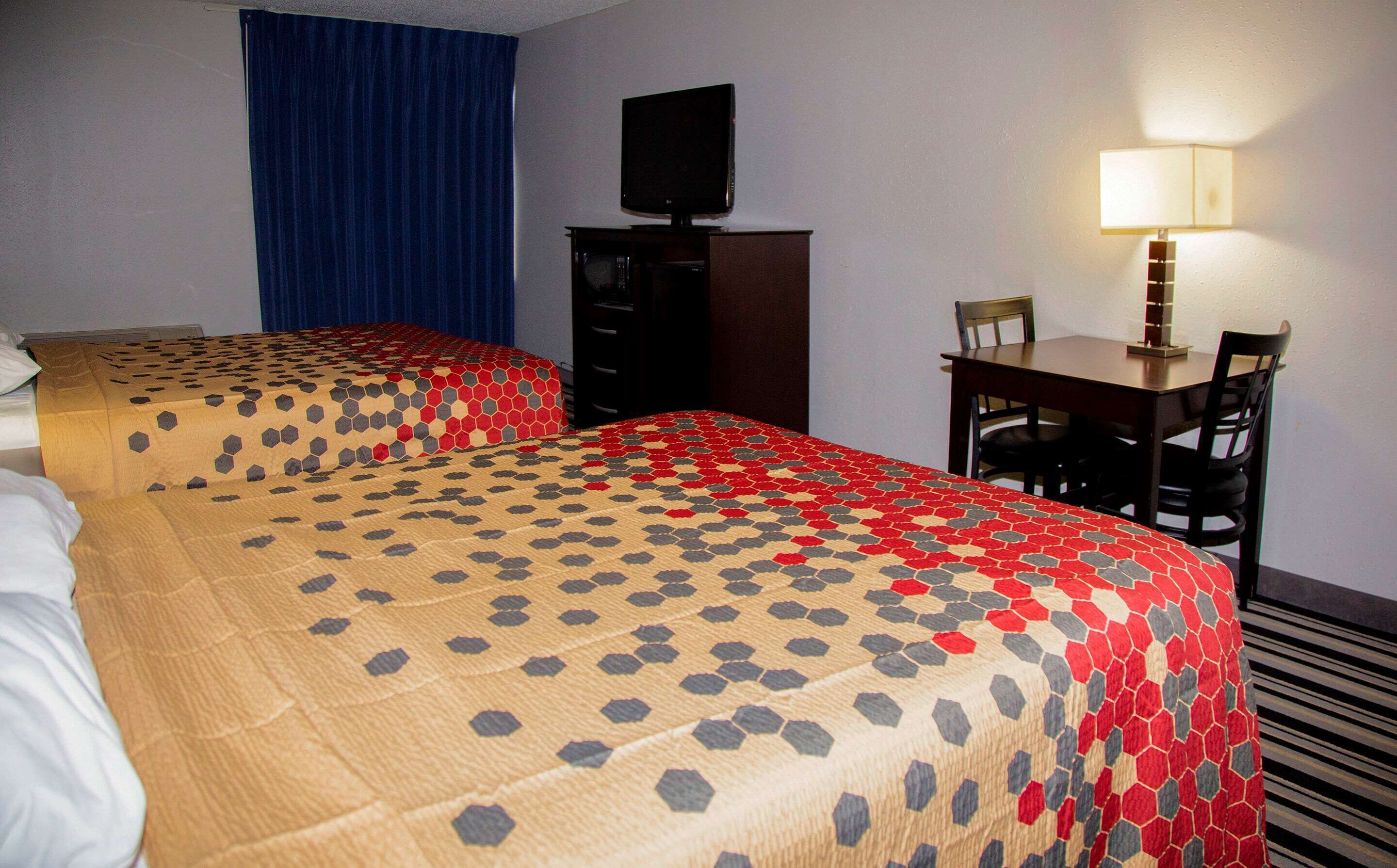 A hotel room with two beds, a desk, a chair, a television, and a lamp.