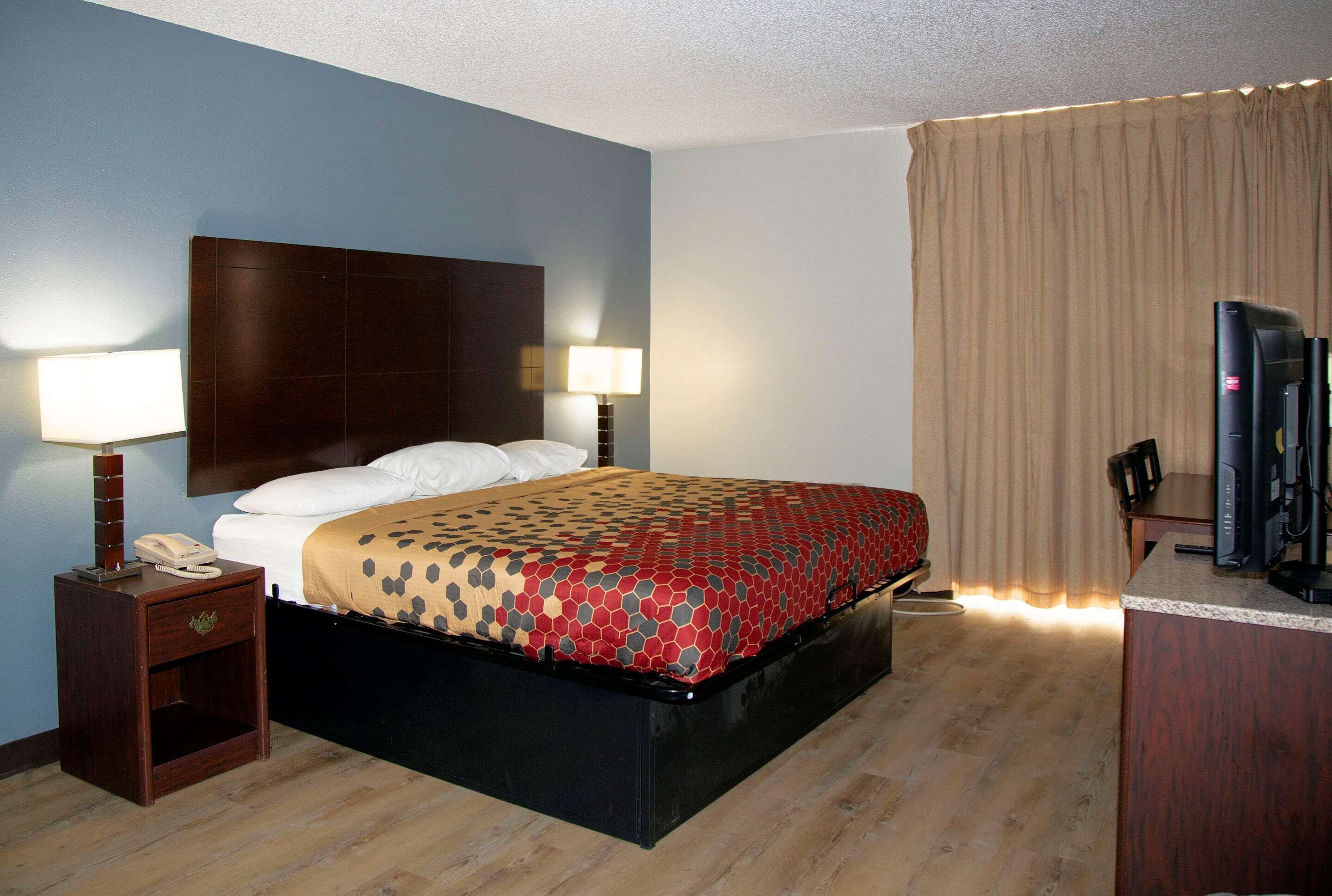 A hotel room with a bed, bedside lamps, a desk with a television, and a window with curtains.
