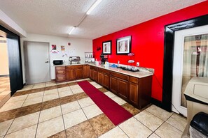A kitchen with wooden cabinets, a red accent wall, and a tiled floor with a red runner. - Econo Lodge Ardmore (Ardmore)