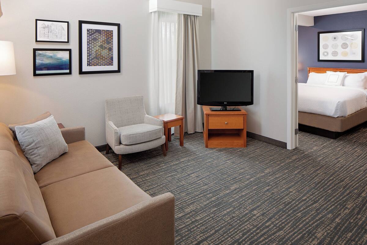 A hotel room with a sofa, armchair, TV, and a bed.