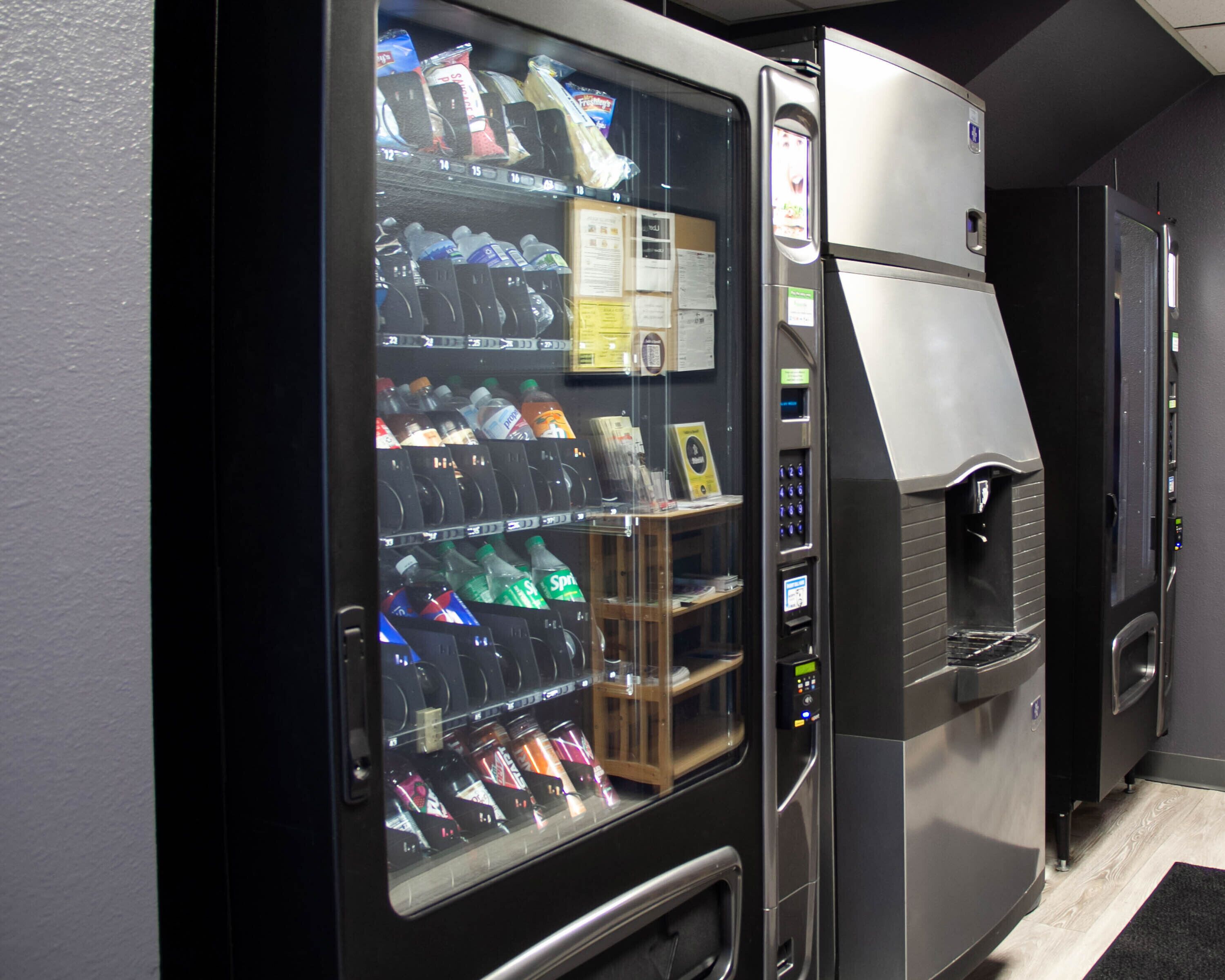 Ein Getränkeautomat mit verschiedenen Getränken und Snacks, ein Bildschirm zur digitalen Bezahlung und ein Kühlschrank mit Wasserspender.