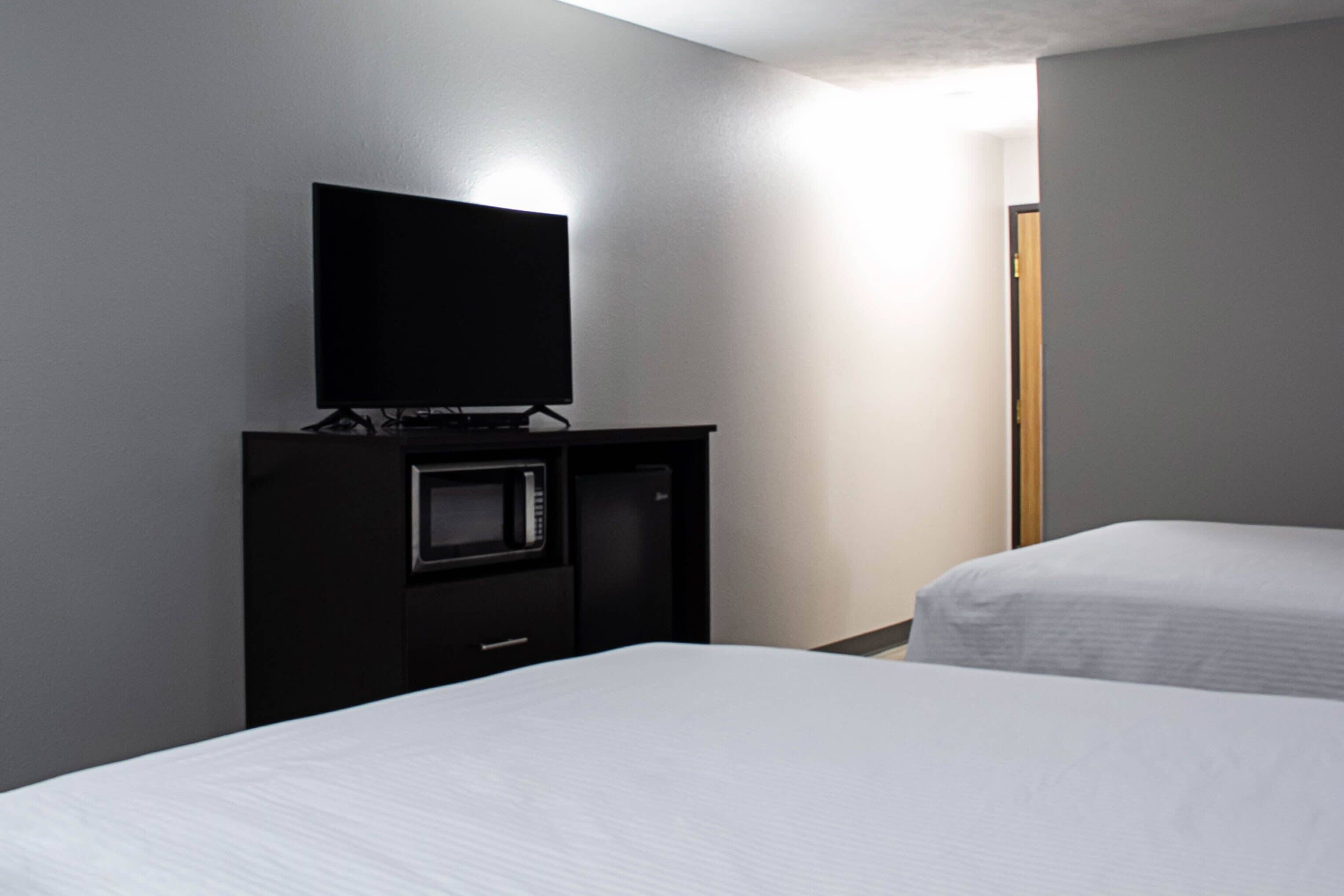 A hotel room with a flat-screen TV, a microwave, and two beds.
