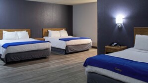 A hotel room with two beds, each with a wooden headboard, white bedding, and a blue accent. There is a nightstand with a phone and a lamp on the wall. - New Victorian Inn Norfolk (Norfolk)