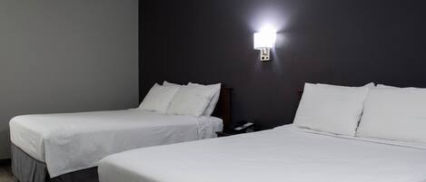 Quarto de hotel com duas camas de solteiro, uma parede escura e um abajur.
