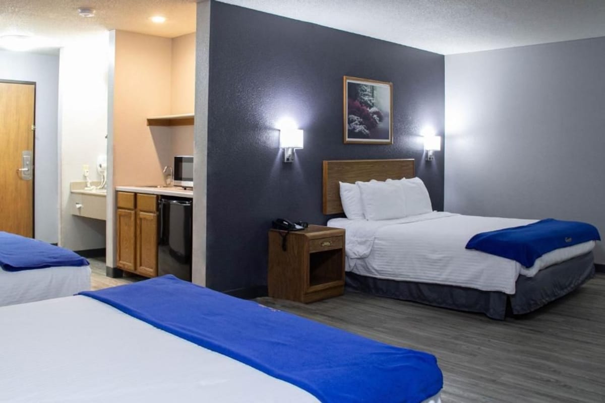 A hotel room with two beds, a small desk with a computer, and a kitchenette.