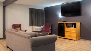 A living room with a sectional sofa, a red armchair, a wooden cabinet with a microwave, and a flat-screen TV mounted on the wall. - New Victorian Inn Norfolk (Norfolk)