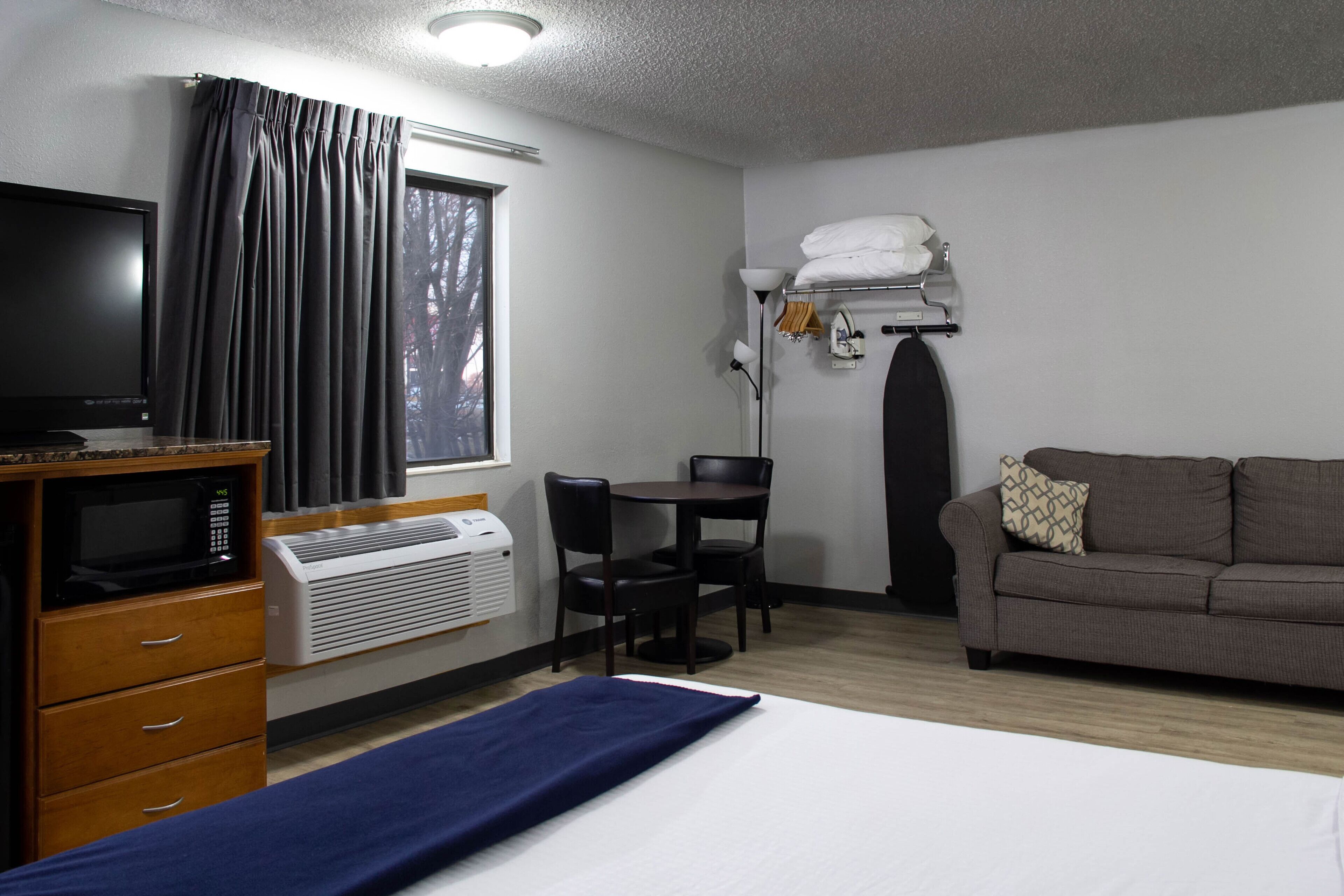 A hotel room with a bed, a desk, a television, a microwave, and a window with curtains.