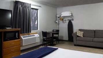 A hotel room with a bed, a desk, a television, a microwave, and a window with curtains.