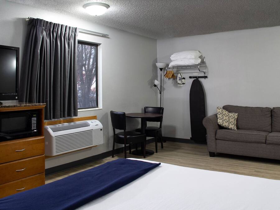 A hotel room with a bed, a desk, a television, a microwave, and a window with curtains.