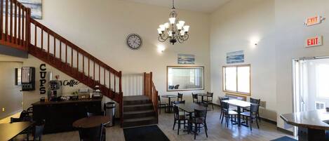A hotel lobby with a staircase, a coffee bar, multiple tables, and chairs.