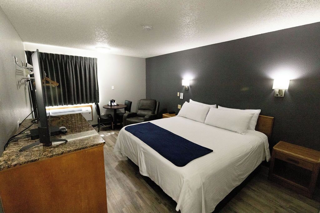 A hotel room with a bed, a desk with a computer, a chair, and a small table.