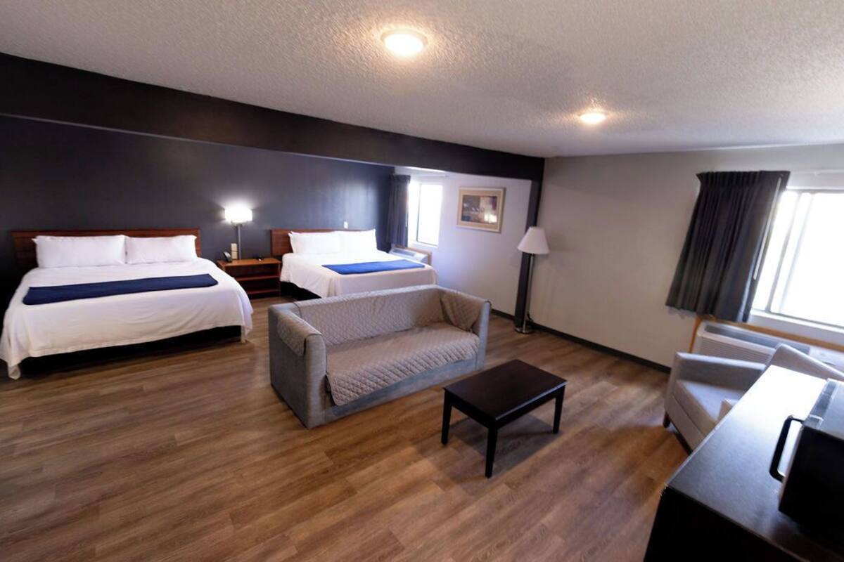 A hotel room with two beds, a sofa, a coffee table, a desk, a lamp, and a window.