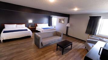A hotel room with two beds, a sofa, a coffee table, a desk, a lamp, and a window.